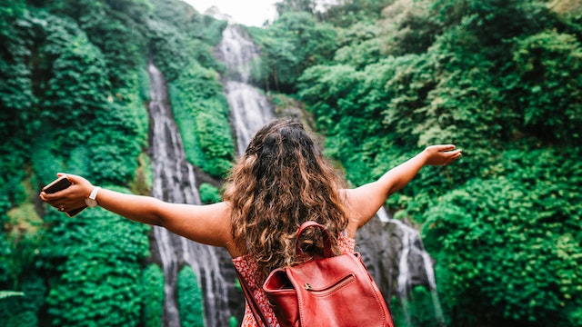 person with their arms outstretched looking at a waterfall surrounded by green spaces